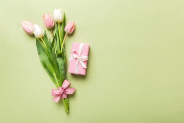 Pembe lale çiçekleri ve hediye ya da renkli masa arkaplanındaki hediye kutusu. Anneler günü, doğum günü, kadınlar günü, kutlama konsepti. Metin üstü görünümü için boşluk.