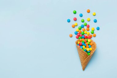 waffle cone full of assorted traditional candies falling out on colored background with copy space. Happy Holidays sale concept.