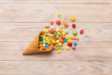 waffle cone full of assorted traditional candies falling out on colored background with copy space. Happy Holidays sale concept.