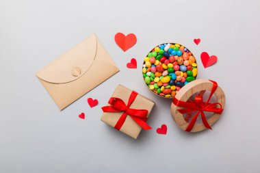 Red envelope with candy and gift box and Valentines hearts on colored background. Flat lay, top view. Romantic love letter for Holiday concept.