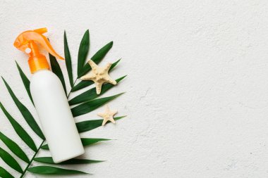 Sunscreen spray bottle. Bottle with sun protection cream and sea shells with tropical green leaf on color background, top view.