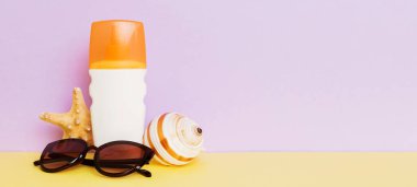 Plaj aksesuarları. Yazın UVB cilt koruması için nemlendirici güneş kremi şişesi ve renkli arka planda deniz kabukları. Kopyalama alanı kullan.