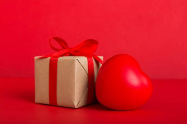 gift box with red bow and red heart on colored background. Perspective view. Flat lay.