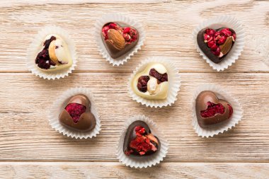 chocolate sweets in the form of a heart with fruits and nuts on a colored background. top view with space for text, holiday concept.