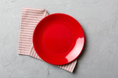 Renkli arka planda üst görünüm yiyecek için masa örtüsü üzerindeki boş yuvarlak kırmızı tabak. Tasarımınız için boşluk olan peçeteye boş tabak.