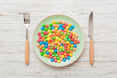 cutlery on table and sweet plate of candy. Health and obesity concept, top view on colored background.