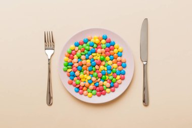 cutlery on table and sweet plate of candy. Health and obesity concept, top view on colored background.