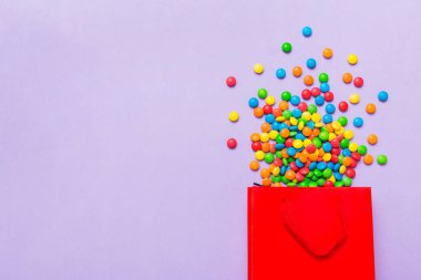 shopping paper gift bag in corner full of assorted traditional candies falling out on colored background with copy space. Happy Holidays sale concept.