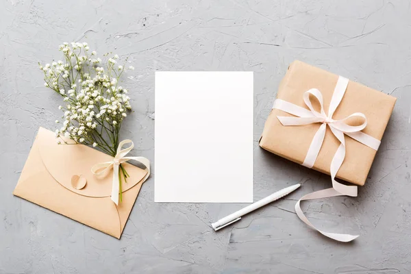 Wedding mockup with white paper list and flowers gypsophila on colored table top view flat lay. Blank greeting cards and envelopes. Beautiful floral pattern. Flat lay style.