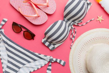 Kadın mayo ve plaj aksesuarları renkli arka plan yaz seyahati konseptine düz bir görünüm kazandırıyordu. Bikini mayo, hasır şapka ve deniz topuklu ayakkabı. Üst görünümü kopyala.