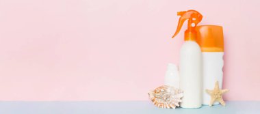 Plaj aksesuarları. Yazın UVB cilt koruması için nemlendirici güneş kremi şişesi ve renkli arka planda deniz kabukları. Kopyalama alanı kullan.