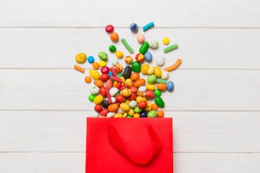 shopping paper gift bag in corner full of assorted traditional candies falling out on colored background with copy space. Happy Holidays sale concept.