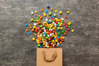 shopping paper gift bag in corner full of assorted traditional candies falling out on colored background with copy space. Happy Holidays sale concept.