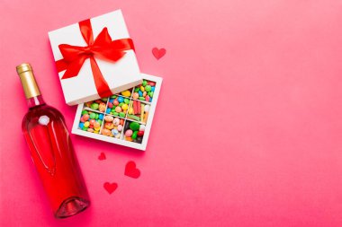 Sevgililer Günü için renkli arka planda bir şişe kırmızı şarap hediye ve çikolatalı. Kalp, hediye kutusuyla şekillendirilmiş çikolatalar fotokopi alanı ile üst görünüm.