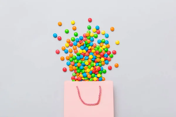 shopping paper gift bag in corner full of assorted traditional candies falling out on colored background with copy space. Happy Holidays sale concept.