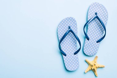 Renkli arka planda parmak arası terlikleri ve deniz kabuğu olan düz bir kompozisyon. Metin üstü görünümü için boşluk.