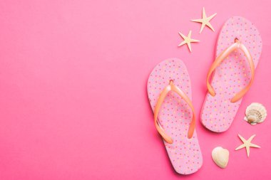 Renkli arka planda parmak arası terlikleri ve deniz kabuğu olan düz bir kompozisyon. Metin üstü görünümü için boşluk.