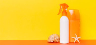 Plaj aksesuarları. Yazın UVB cilt koruması için nemlendirici güneş kremi şişesi ve renkli arka planda deniz kabukları. Kopyalama alanı kullan.