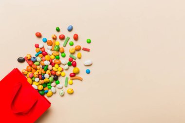 shopping paper gift bag in corner full of assorted traditional candies falling out on colored background with copy space. Happy Holidays sale concept.
