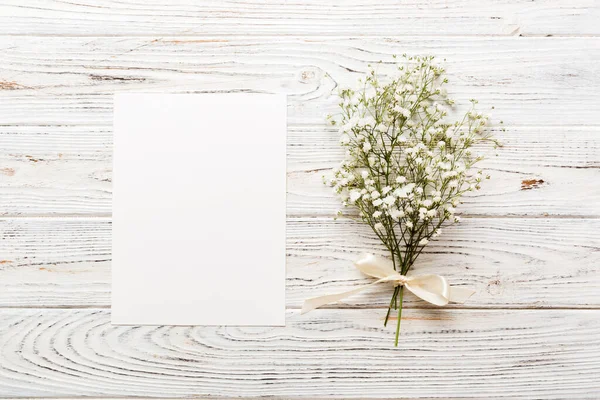 Wedding mockup with white paper list and flowers gypsophila on colored table top view flat lay. Blank greeting cards and envelopes. Beautiful floral pattern. Flat lay style.