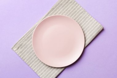 Renkli arka planda üst manzara. Yemek için masa örtüsü üzerine yuvarlak pembe tabak. Tasarımınız için boşluk olan peçeteye boş tabak.