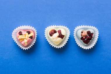 chocolate sweets in the form of a heart with fruits and nuts on a colored background. top view with space for text, holiday concept.