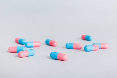 Heap of pink and blue pills on colored background. Tablets scattered on a table. Pile of red soft gelatin capsule. Vitamins and dietary supplements concept.