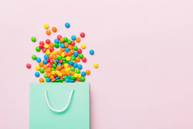 shopping paper gift bag in corner full of assorted traditional candies falling out on colored background with copy space. Happy Holidays sale concept.