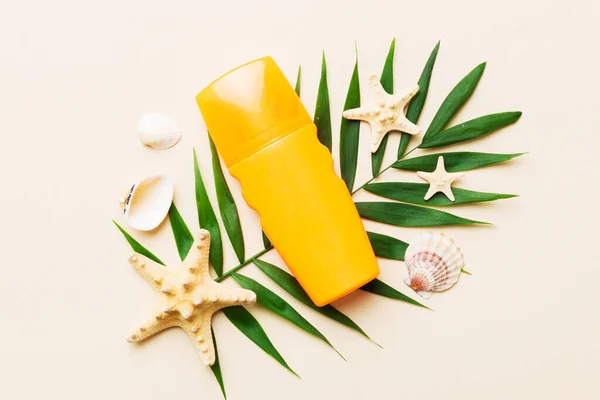 stock image Sunscreen spray bottle. Bottle with sun protection cream and sea shells with tropical green leaf on color background, top view.