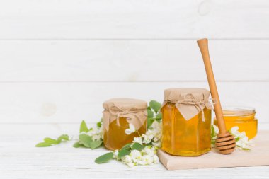 Tatlı bal kavanozu bahar akasyası çiçeklerini sarmıştı. Kavanozdaki kaşıktan bal akar. Tahta zemin üzerinde taze akasya balı kavanozları.