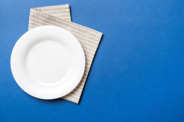 Renkli arka planda üst görünüm yiyecek için masa örtüsü üzerindeki boş yuvarlak beyaz tabak. Tasarımınız için boşluk olan peçeteye boş tabak.
