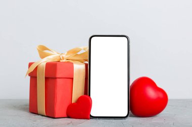 mobile phone with blank screen on colored background with hearts, calendar and gift box, valentine day concept perspertive view flat lay.