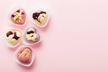 chocolate sweets in the form of a heart with fruits and nuts on a colored background. top view with space for text, holiday concept.