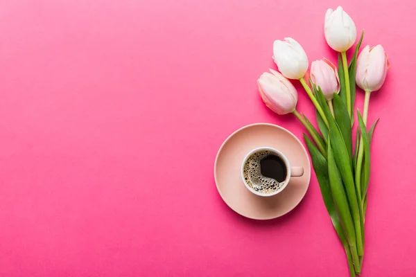 stock image Spring background with flowers, a cup of coffee and a bouquet of pink and white tulips on colored table background with place for text. Copy space top view.