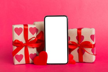 mobile phone with blank screen on colored background with hearts, calendar and gift box, valentine day concept perspertive view flat lay.