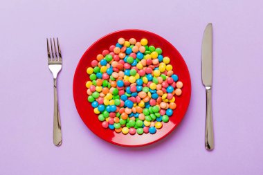 cutlery on table and sweet plate of candy. Health and obesity concept, top view on colored background.