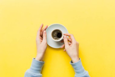 Renkli arka planda bir fincan kahve tutan minimalist stil bir kadın. Düz yerde, kapuçino bardağının üstünde. Metin için boş yer, kopyalama alanı. Kahve bağımlılığı. Üst manzara, düz uzanma.