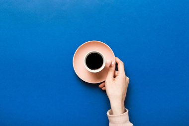 Renkli arka planda bir fincan kahve tutan minimalist stil bir kadın. Düz yatıyordu, üstten espresso fincanı. Metin için boş yer, kopyalama alanı. Kahve bağımlılığı. Üst manzara, düz uzanma.