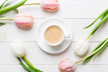 Çiçeklerle dolu bahar arkaplanı, bir fincan kahve ve renkli masa arkaplanlı pembe ve beyaz laleler. Üst görünümü kopyala.