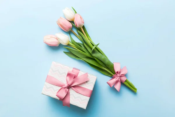 Pink tulips flowers and gift or present box on colored table background. Mothers Day, Birthday, Womens Day, celebration concept. Space for text top view.