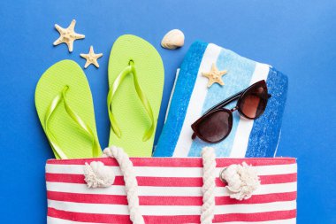 Plaj aksesuarları renkli arka plan yaz seyahati konseptinde düz bir görünüm sergiliyordu. İçinde deniz yıldızı ve deniz kabuğu olan bir çanta. Üst görünüm.