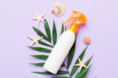 Sunscreen spray bottle. Bottle with sun protection cream and sea shells with tropical green leaf on color background, top view.