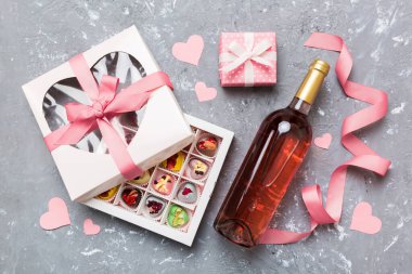 Sevgililer Günü için renkli arka planda bir şişe kırmızı şarap hediye ve çikolatalı. Kalp, hediye kutusuyla şekillendirilmiş çikolatalar fotokopi alanı ile üst görünüm.