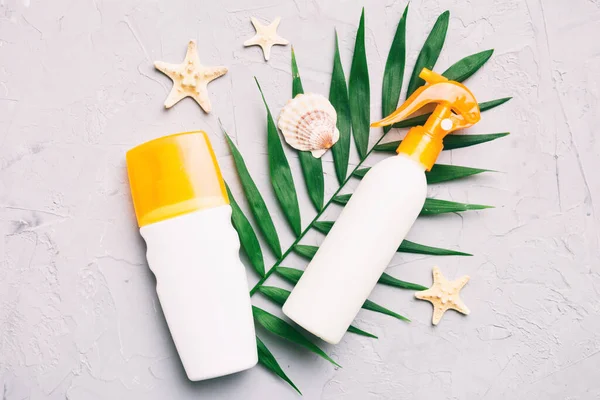 stock image Sunscreen spray bottle. Bottle with sun protection cream and sea shells with tropical green leaf on color background, top view.