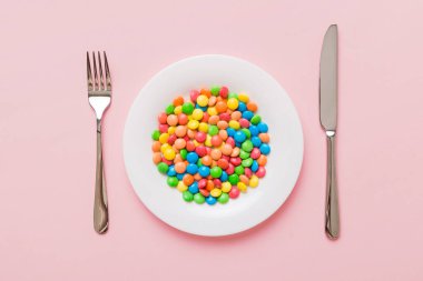 cutlery on table and sweet plate of candy. Health and obesity concept, top view on colored background.