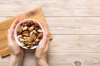 Kadın elleri, fındıklı, fıstıklı, bademli, fındıklı ve fındıklı ahşap bir kase tutuyor. Sağlıklı yemek ve atıştırmalık. Farklı fındıklı vejetaryen atıştırmalıkları..