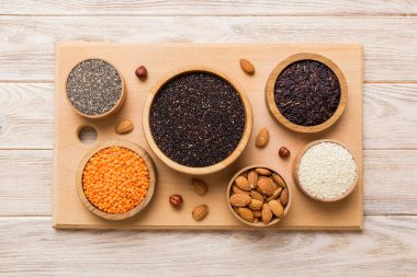 Smal Bowl 'da renkli arka planda çeşitli süper yiyecekler. Pirinç, chia, kinoa, mercimek, fındık, susam tohumu, badem gibi süper yiyecekler. en üstteki görünüm.