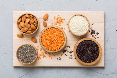 Smal Bowl 'da renkli arka planda çeşitli süper yiyecekler. Pirinç, chia, kinoa, mercimek, fındık, susam tohumu, badem gibi süper yiyecekler. en üstteki görünüm.