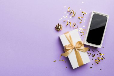 Altın kurdeleli hediye kutusu ve arka planda akıllı telefon, üst manzara. Boş kutu paketleme modeli, tasarımınız için şablon - markalaşma modeli.