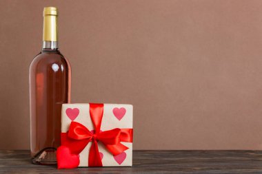 Bottle of wine on colored background for Valentine Day with gift box. Heart shaped with presrnt box perspective view with copy space.